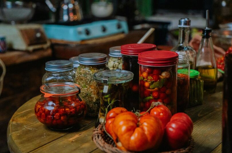 A cozy indoor kitchen setup featuring various preserved vegetables in jars, alongside fresh produce.